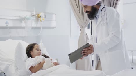 happy biracial doctor using tablet with sick girl patient in hospital bed in slow motion