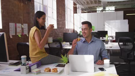 Diverse-male-and-female-business-colleagues-eating-pastries-and-smiling