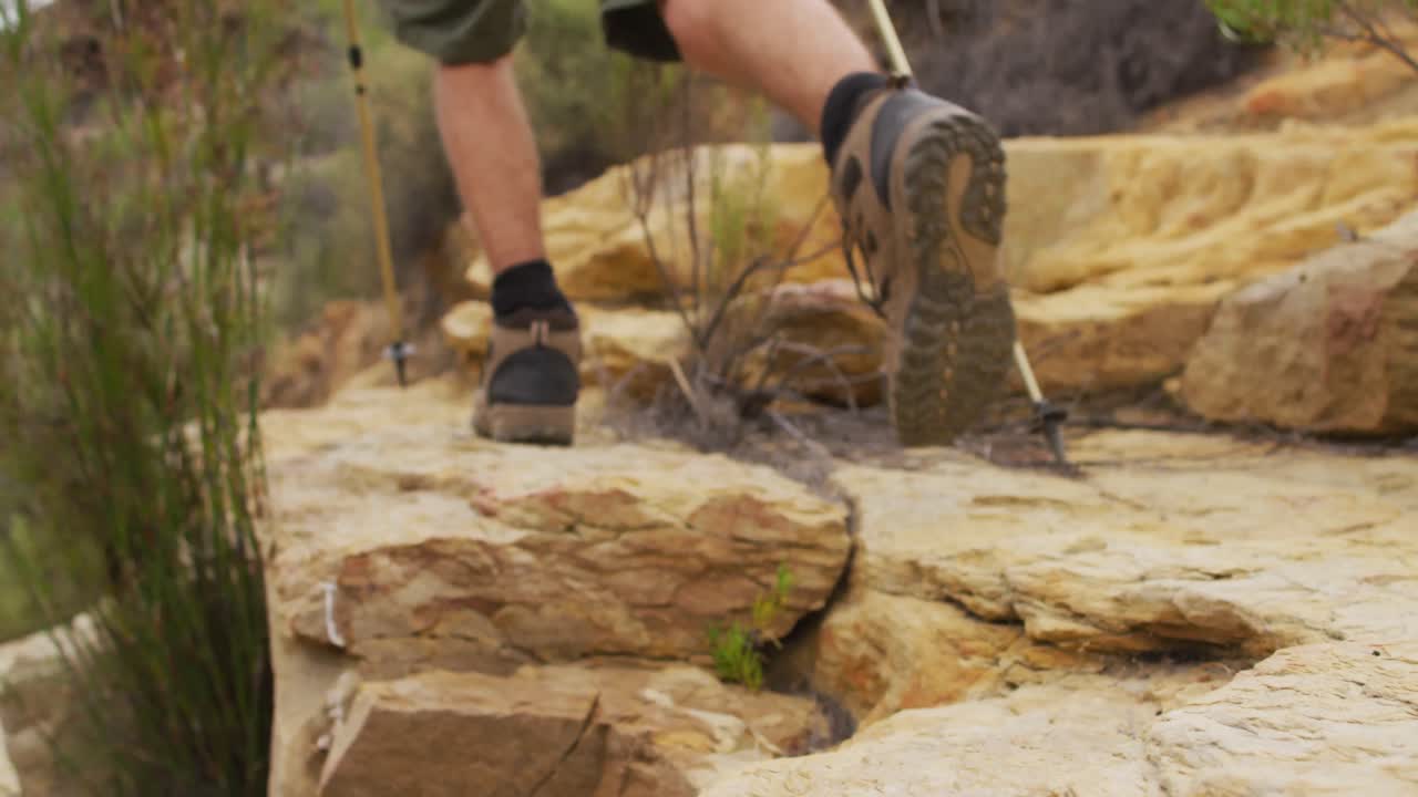 Feet of male survivalist trekking across rocky terrain in walking boots and using walking poles