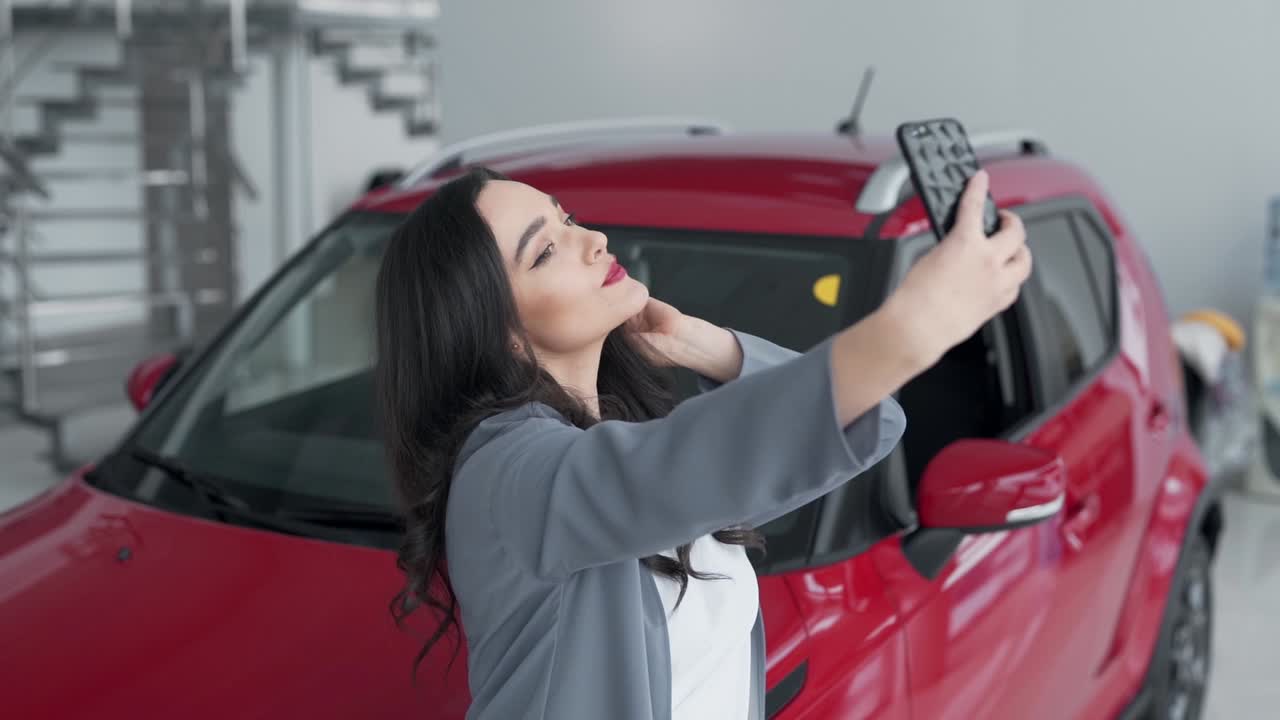 hermosa joven tomando un selfie en un concesionario de automóviles con un automóvil rojo
