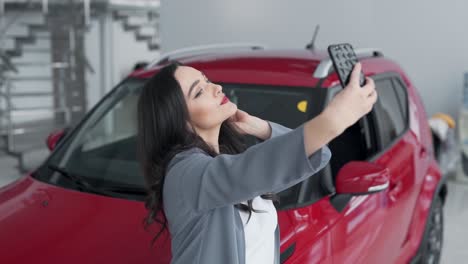 Hermosa-Joven-Tomando-Un-Selfie-En-Un-Concesionario-De-Automóviles-Con-Un-Automóvil-Rojo