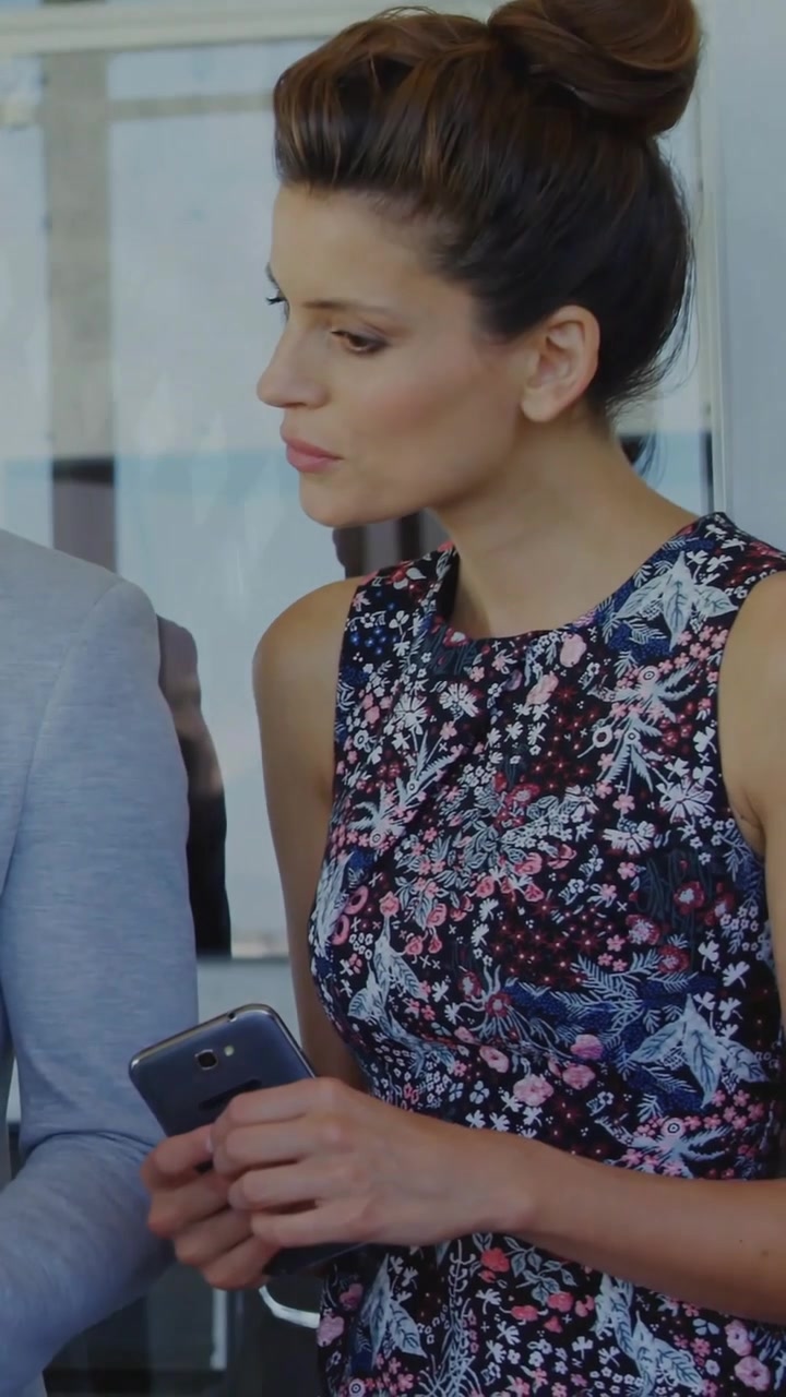 Video verticale: donna con il telefono che guarda una presentazione, mostrando grafici aziendali su una superficie di vetro mentre analizza.