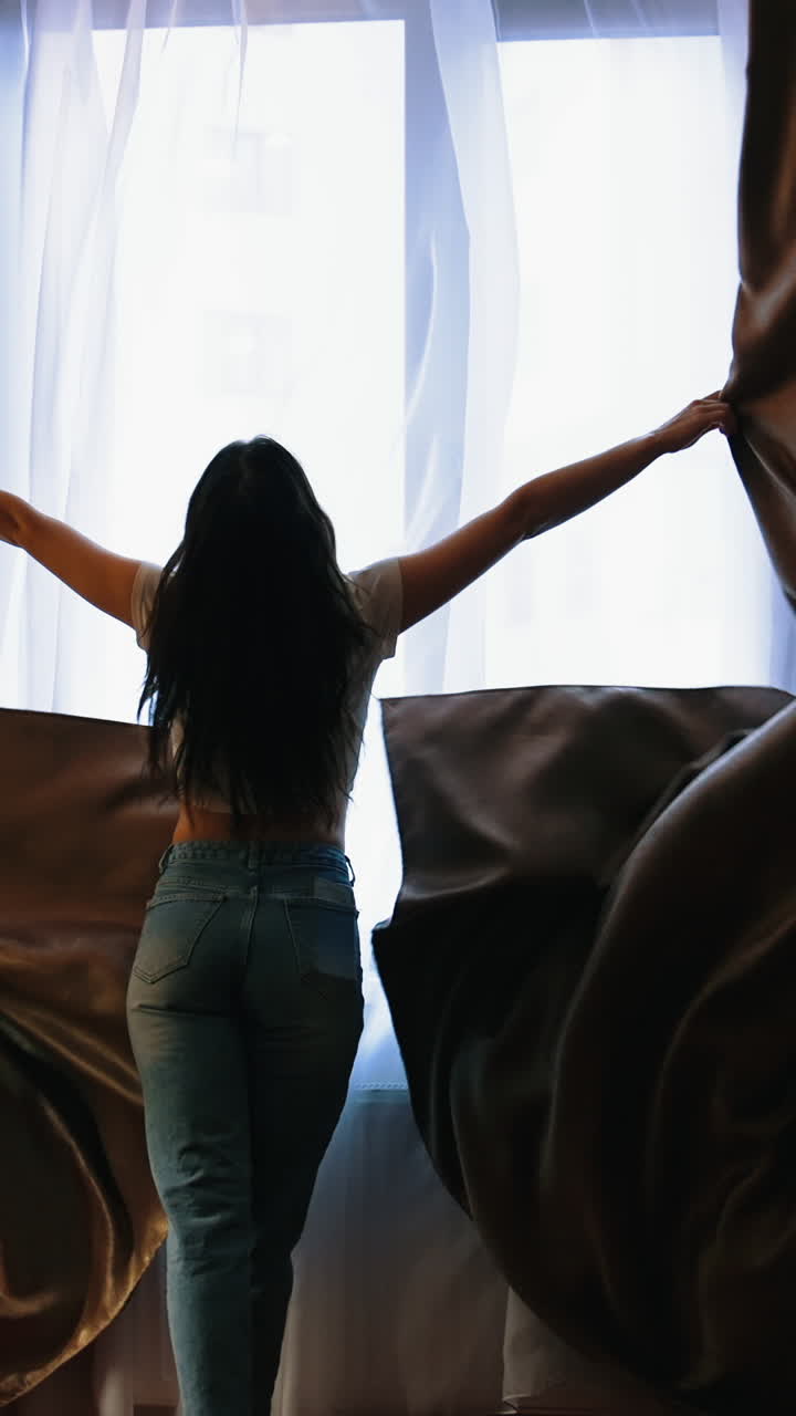 Happy optimistic young woman opens window. Smiling girl running happily to the window and opening dark curtains in luxury hotel room. Vertical video