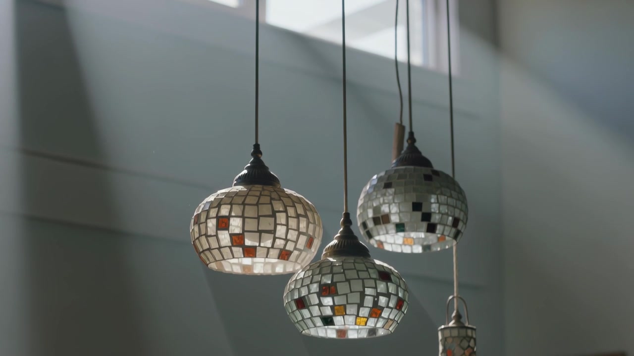 Skinnende mosaikklamper fanger solstråler fra overlysvinduer, og skiftende høydepunkter danser over en blek vegg.