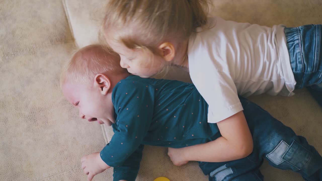 예쁜 소녀는 울고 있는 아기 동생을 진정시켜 큰 침대에  ⁇ 습니다.