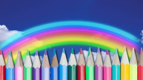 varios lápices de colores contra el arco iris en el cielo azul