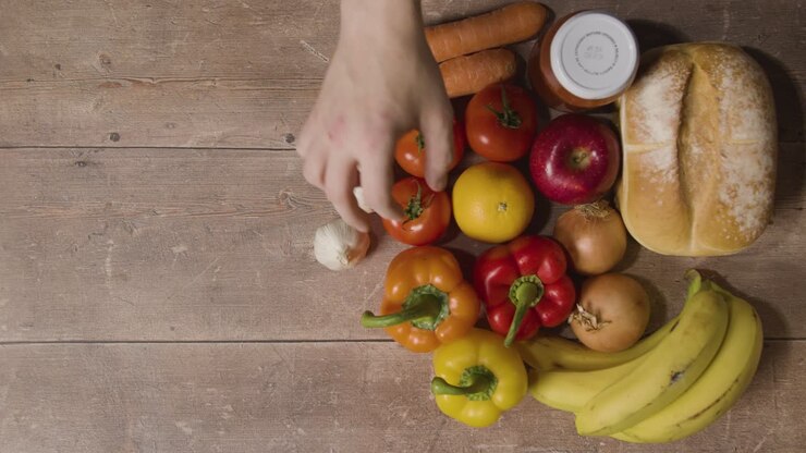 Overhead Shot Of Person Putting Tomato Into Group Of Fresh Food Items On Wooden Surface