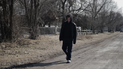 a young high school aged teen boy wearing a backpack walking down a road during the winter on a cold day