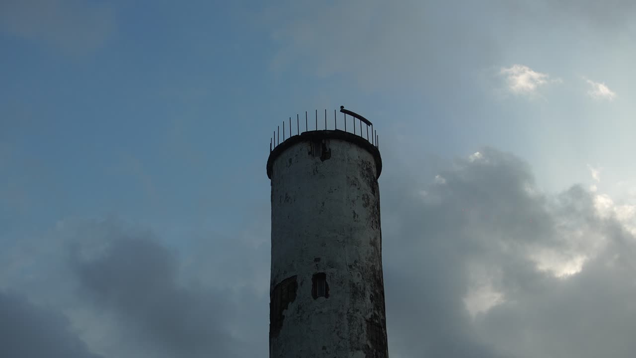 Weathered Harrinniemi lighthouse rises against a dramatic cloudy sky, showing age and character