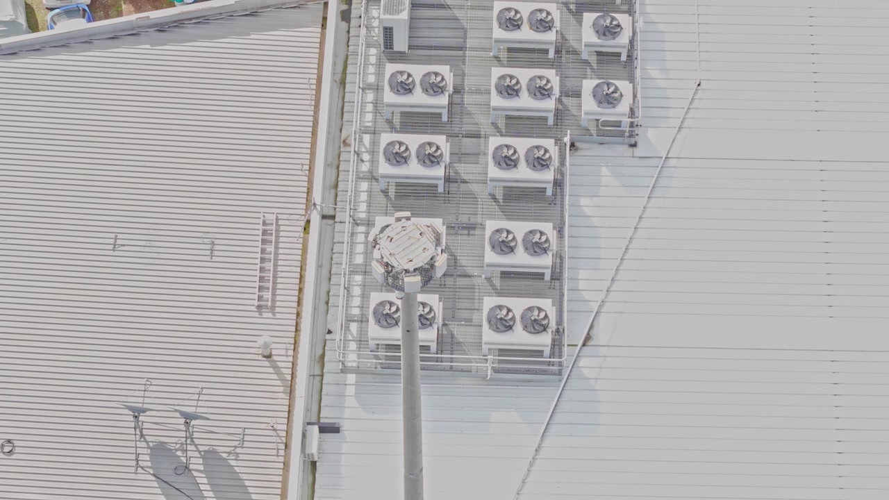 Drone shot of a modern data centre rooftop featuring multiple HVAC cooling units, clean metal surfaces, bright daylight, geometric layout, and industrial equipment. No people present.