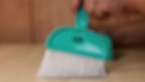 hand using brush to clean wooden desk