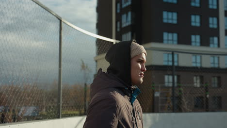 young man walks into sports arena with light rays shining around him, featuring background with residential building, parked cars, and a fence