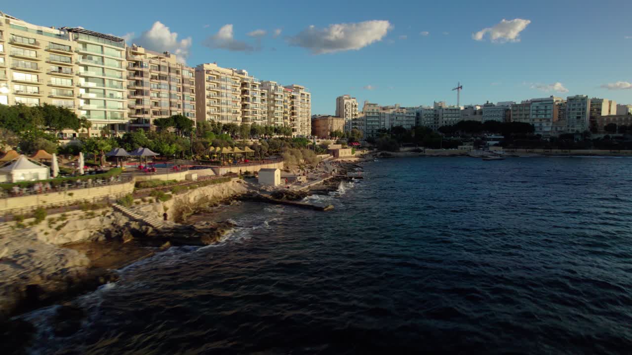 Fast FPV drone shot flying along rocky Sliema coast with buildings and waves