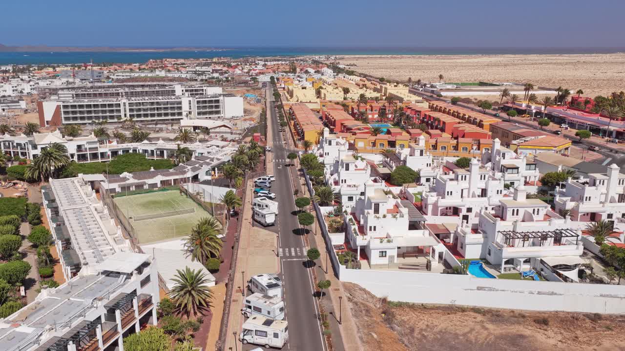 Corralejo’s coastal zone near Acua Water Park with white buildings, tennis courts, palm-lined roads, and desert terrain showing resort planning and urban sprawl in northern Fuerteventura