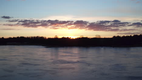 stunning cinematic aerial shot flying over a frozen lake towards sunset