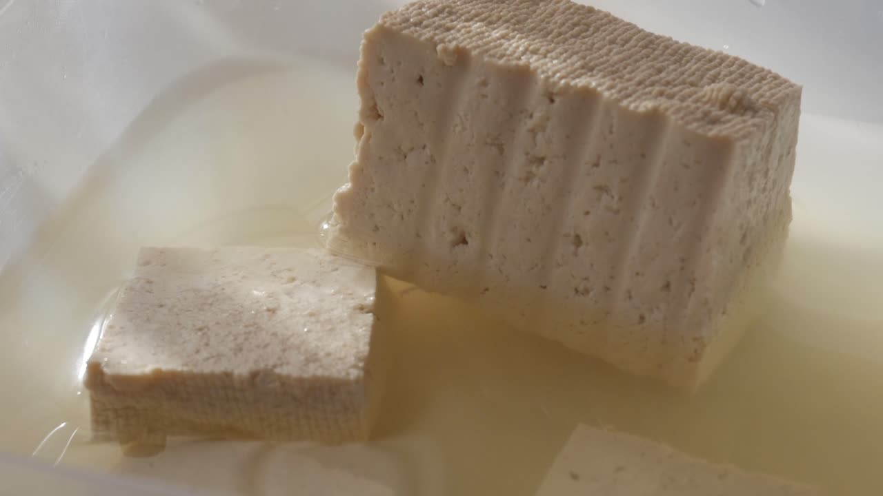 Blocks of tofu soaking in water inside a clear container, soft morning light