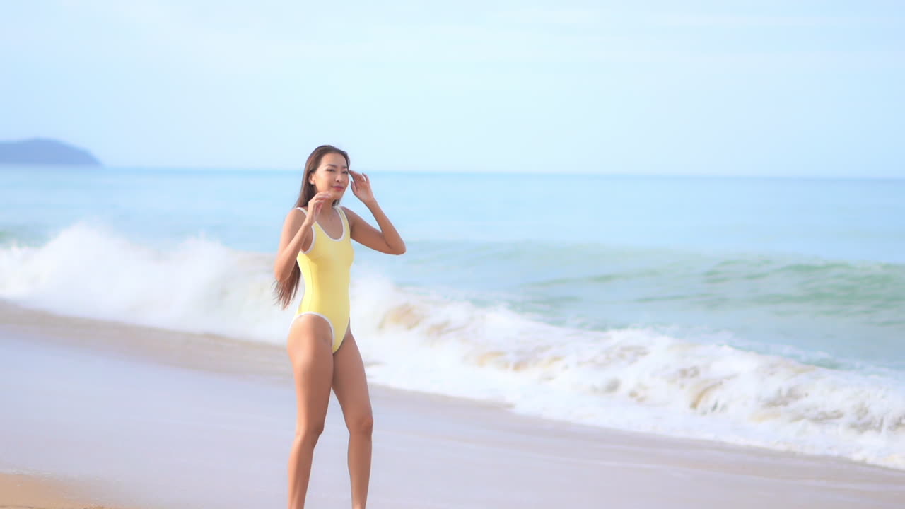 수영복을 입은 아름답고, 건강하고, 건강한 여성이 포효하는 파도를 향해 걷고, 돌아서서 해안선을 따라 걷습니다.