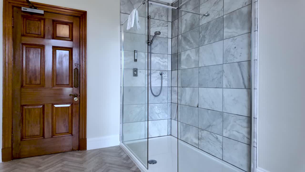 Modern Bathroom Interior With Walk-In Shower Featuring Glass Enclosure And Marble Tile Alongside Wooden Door And Herringbone Floor Design In Residential Setting