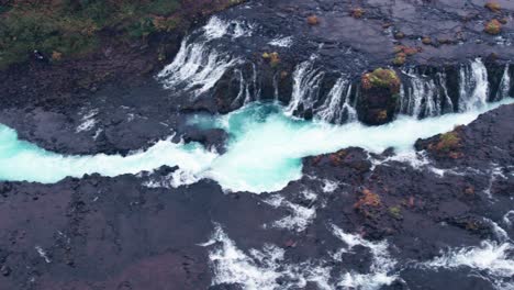 aerial: side angle of bruarfoss cascading waterfall off the golden circle in southern iceland that is very picturesque with the beautiful blue cascade of falls into the plunge pool below