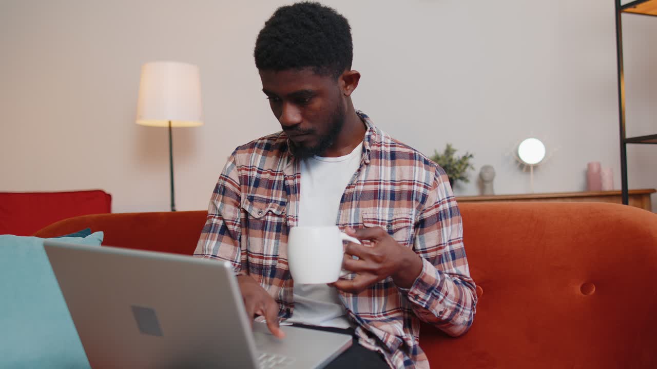 Young man using laptop computer lying on sofa at home working online shopping from home office