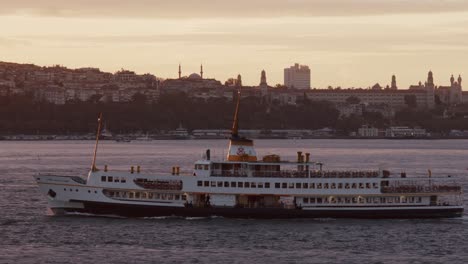 a passenger ship sailing through bosphorus strait with istanbul city buildings in background at sunset, turkey