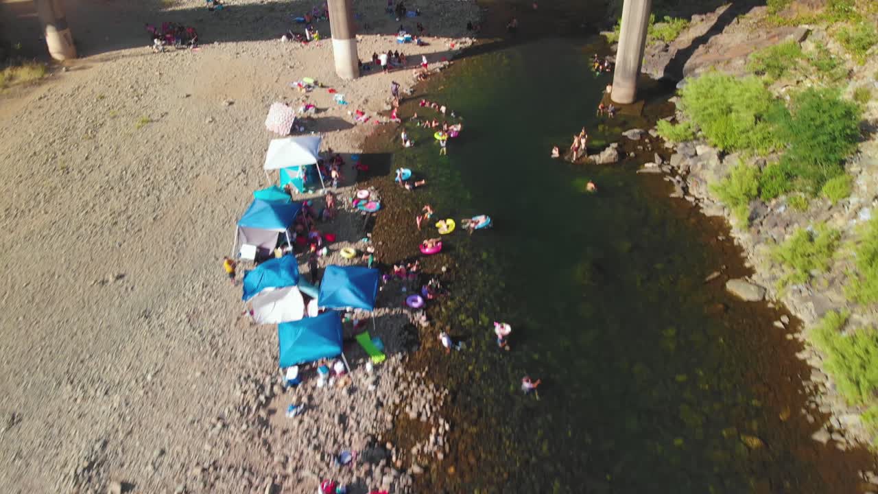 푸른 나무로 둘러싸여 있고 수영과 여름 주말을 즐기는 사람들로 가득한 캘리포니아의 아메리칸 강에 있는 오번 수영 구멍을 가로지르는 다리를 가까이서 볼 수 있습니다.