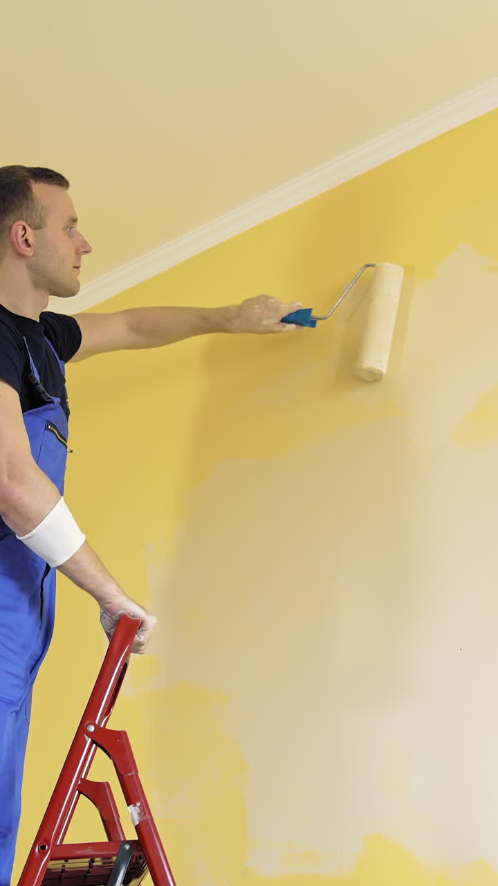 Young painter doing house renovation. Handsome worker painting new wall. Vertical video
