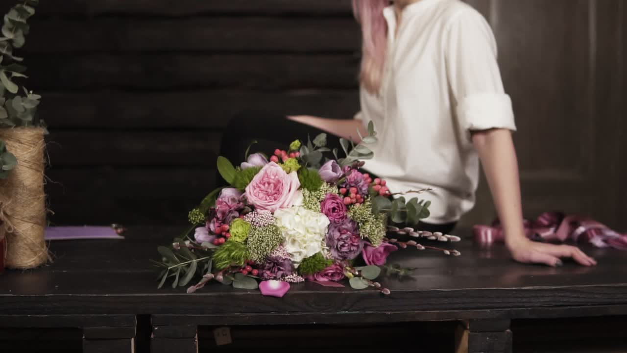 hermosas imágenes en cámara lenta de un increíble ramo hecho por un florista profesional. seductora, sonriente chica con camisa blanca está sentada en la mesa. estudio