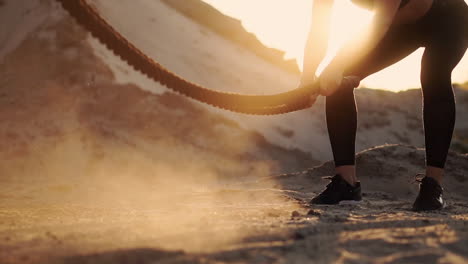 Close-up-of-a-girl-with-a-rope-conducts-outdoor-training-on-the-sandy-ground-near-the-beach.-Rope-in-the-hands-of-women-at-sunset