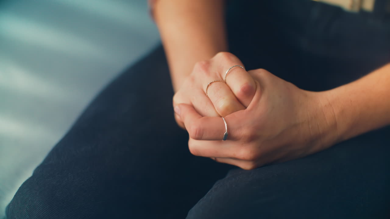 Nervous hands of a woman sitting on a blue therapy office sofa receives distressing news. Ideal for mental health awareness campaigns, counseling resources, and dramatic storytelling