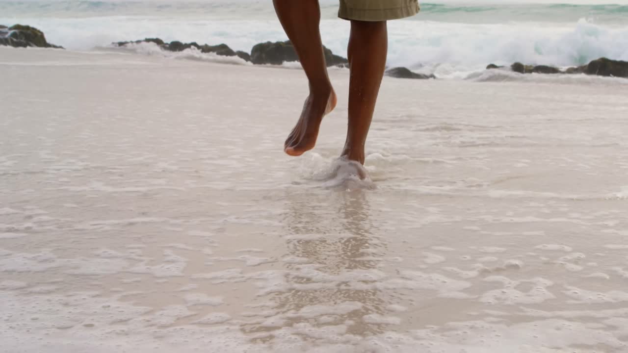 sección baja de un hombre caminando descalzo en la playa en un día soleado 4k