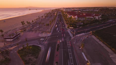 El-Ajetreo-Y-El-Bullicio-De-La-Hora-Pico-En-La-Intersección-Del-Bulevar-De-La-Playa-Y-La-Autopista-De-La-Costa-Del-Pacífico-En-Este-Vibrante-Lapso-De-Tiempo-De-Drones,-Que-Muestra-Los-Colores-Cambiantes-Al-Atardecer-Frente-A-La-Vista