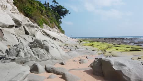 da dietro una roccia gessosa a una vista completa dell'insolita spiaggia di un'isola tropicale remota con la bassa marea nel mare delle andamane