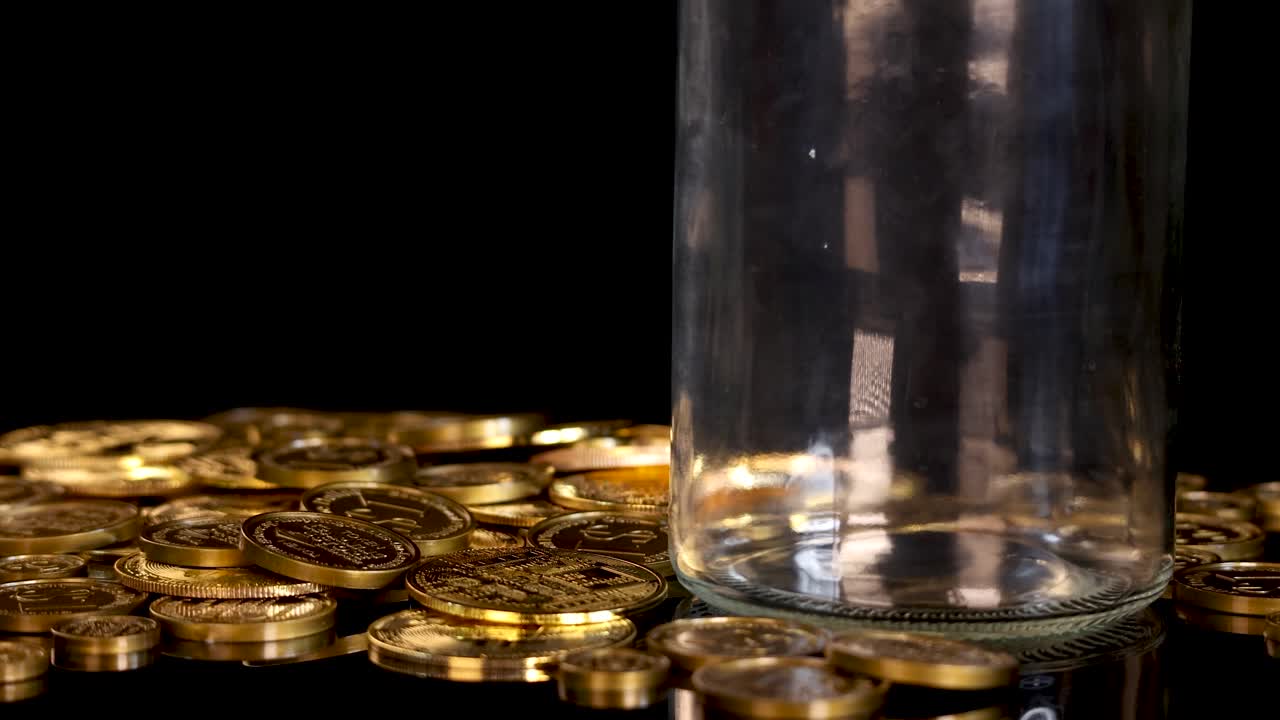 Bitcoin tokens fall into a glass jar surrounded by gold coins under studio lighting