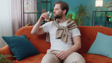 thirsty caucasian man sitting at home holding glass of natural aqua make sips drinking still water