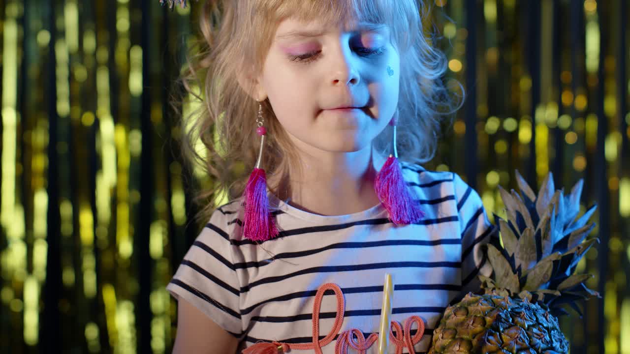 아나나스 과일과 함께 유행하는 스타일리시한 어린이 아이는 네온 조명과 함께 미래의 클럽에서 주스를 마시고 있습니다.