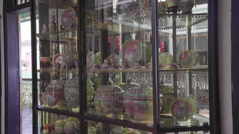 colourful flowers on the round table and beautiful ceramic potteries inside the glass shelf at pinang peranakan mansion in penang malaysia - panoramic shot