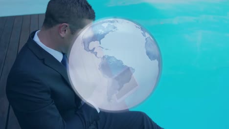 Animation-of-blue-and-white-globe,-over-businessman-using-tablet-by-pool