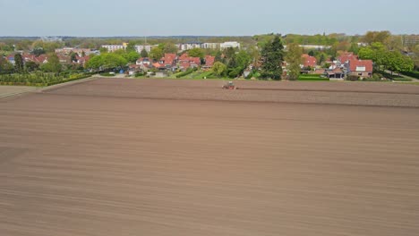 Aerial-of-tractor-plowing-a-plot-of-dirt-at-the-edge-of-a-small-town