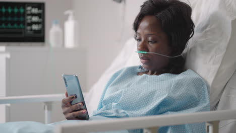 a young woman writes a message on her phone while lying in a hospital ward. an african girl is lying in a ward connected to ecg and oxygen devices in a mask and writes messages to relatives