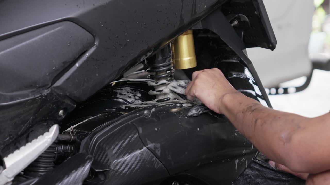 Person cleaning a motorcycle with a cloth, close-up of a shiny black frame
