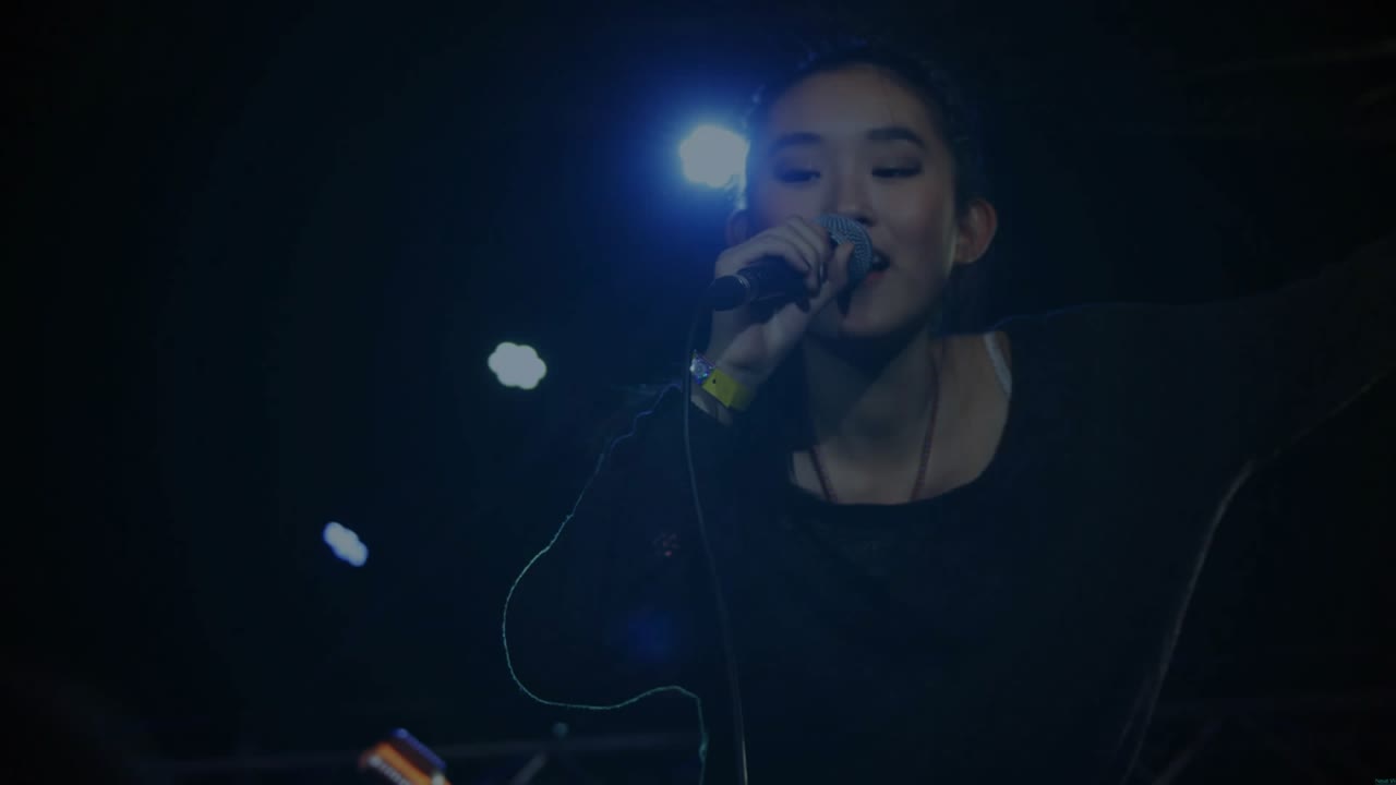 Spotlight cue launching female singer singing into mic at concert, engaging crowd, sparking bokeh