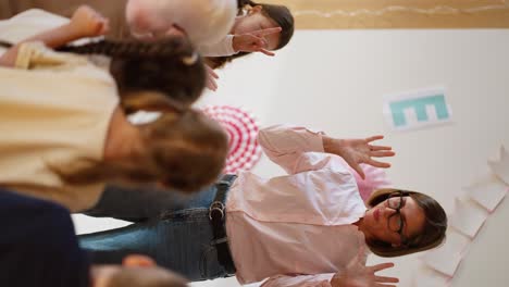 Vertikales-Video-Einer-Frau-Mit-Bob-Frisur,-Brille-Und-Rosa-Hemd,-Die-In-Einem-Speziellen-Club-Zur-Vorbereitung-Der-Kinder-Auf-Die-Schule-Ein-Aufwärmtraining-Für-Vorschulkinder-Macht