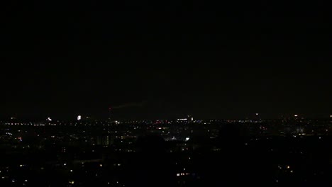 Two-silhouettes-of-people-standing-on-top-of-hill,-overlooking-city-night-skyline-with-fireworks