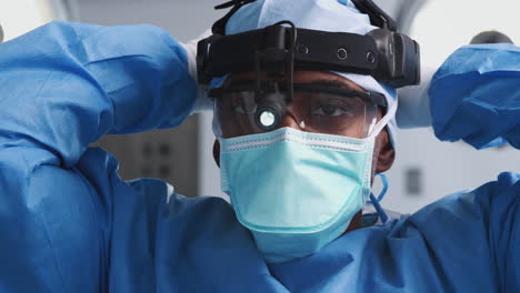 male surgeon with protective glasses and head light putting on mask in hospital operating theater