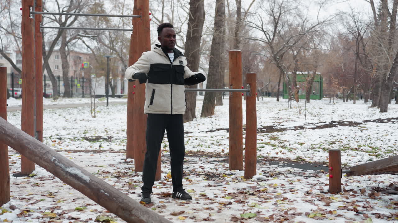 어린 소년은 겨울에 야외에서 팔을 는 운동을 하며, 눈과 운동 장비, 배경의 나무와 도시 환경으로 둘러싸여 있습니다.