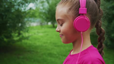 a young girl enjoying music in a lush green park with stylish pink headphones while radiating joy and contentment in nature's embrace