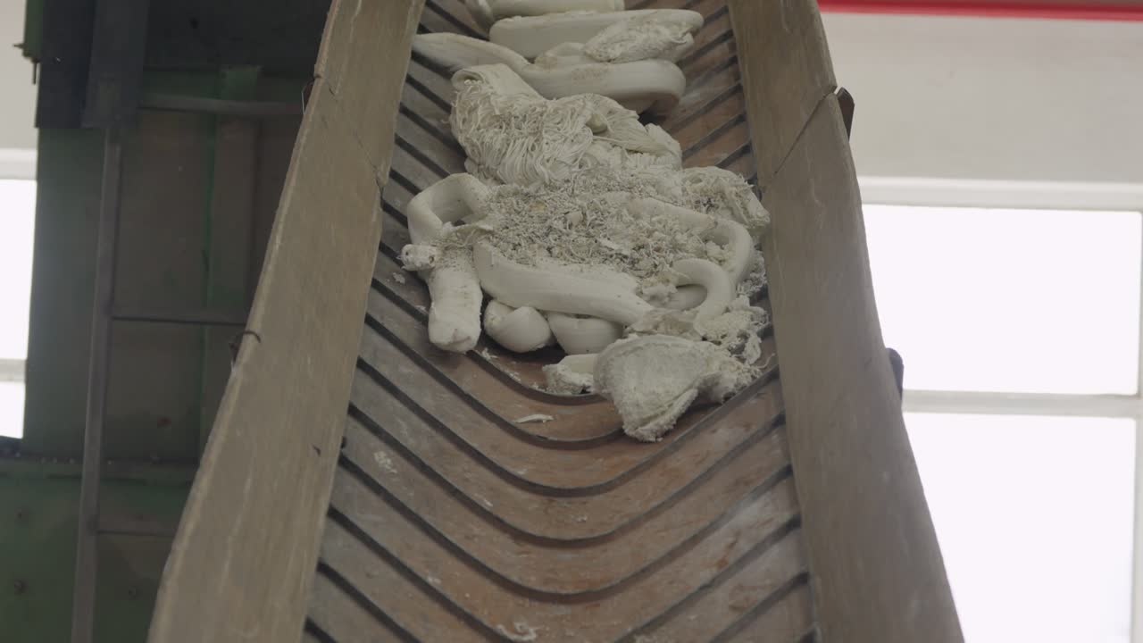 White extruded plastic tubes strips and shavings collected on wooden slatted conveyor belt in recycling facility