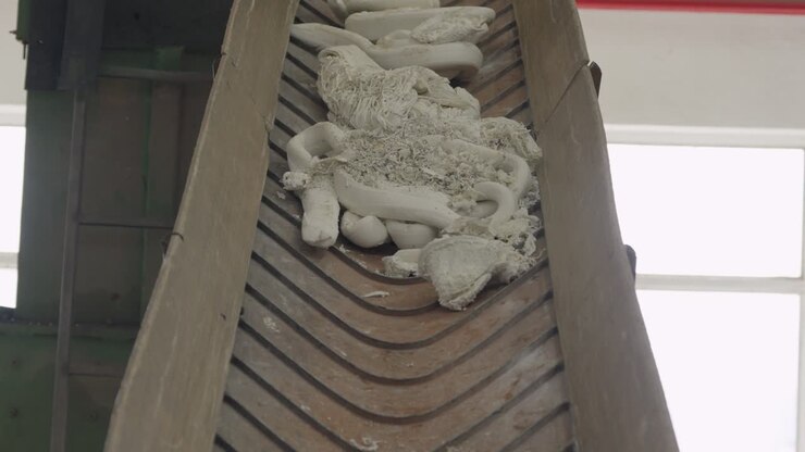 White extruded plastic tubes strips and shavings collected on wooden slatted conveyor belt in recycling facility
