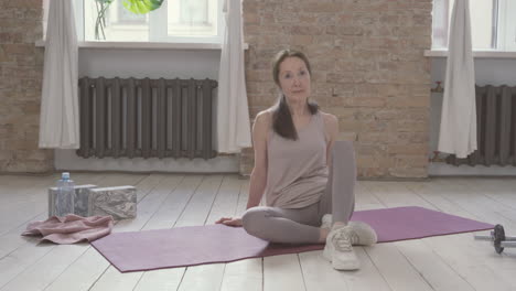 old female ties her shoelaces sitting on yoga mat at home